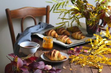 Cozy Autumn Still Life, Freshly Baked Croissants with Cinnamon and Salted Caramel, Cup of Tea and Fall Leaves on Wooden Table