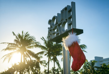 Santa's Christmas stocking hanging from South Beach sign in Miami with a tropical palm tree sunrise...
