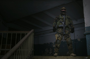 Military army soldier in camouflage is standing with assault rifle inside captured building.