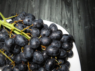Bunches of black grapes in a plate on a wooden table, healthy food