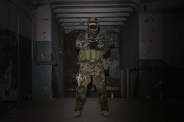 Military army soldier in camouflage is standing with assault rifle inside captured building.