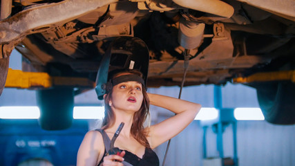 Mechanic girl in a opened helmet holding a welding machine.