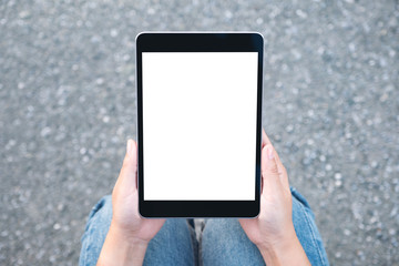 Top view mockup image of a woman holding black tablet pc with blank white screen while sitting on the street background