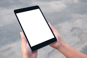 Mockup image of hands holding black tablet pc with blank white screen with street background