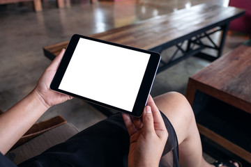 Mockup image of a woman sitting and holding black tablet pc with blank white desktop screen in wooden cafe