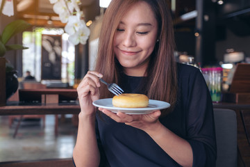 A beautiful asian woman holding a fork to cut a piece of donut with feeling happy in cafe