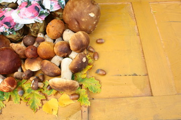 Świeżo zebrane prawdziwki, marynowane grzyby w słoikach, żołędzie i dębowe liście na żółtych deskach, jesiene tło - obrazy, fototapety, plakaty