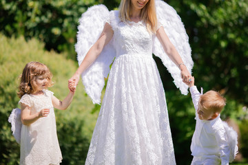 Beautiful mother and her toddler son and daughter wearing angel costumes. Cheerful moment, loving...