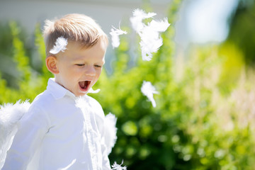 Adorable toddler boy in angel costume playing with white feathers, angelic child.