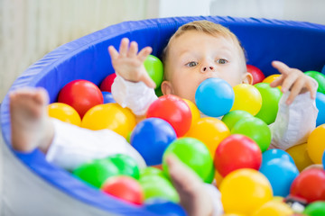 Fototapeta na wymiar Adorable little boy having fun in the pool with colourful plastic balls