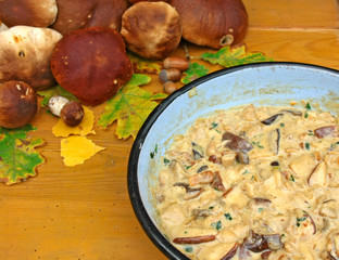 Frying pan full of mushroom sauce, mushrooms and autumn leaves on wooden boards