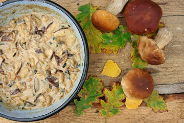 Patelnia pełna grzybowego sosu, grzyby i jesienne liście na drewnianych deskach © Monika