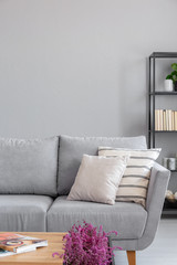Pillows on grey couch in minimal living room interior with copy space on empty wall. Real photo