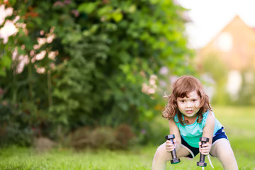 Happy little girl lifting dumbbells in the park