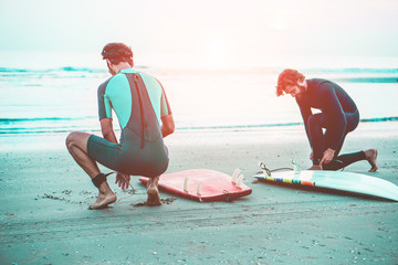 Young surfers preparing the gear equipment on the beach at sunset