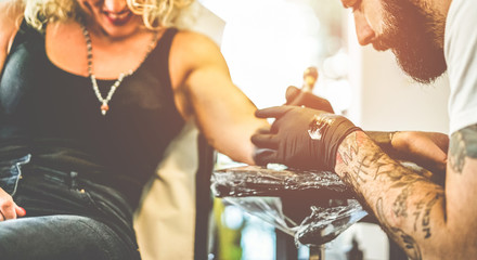 Professional bearded tattoo artist making tattoo in his ink studio on blond woman