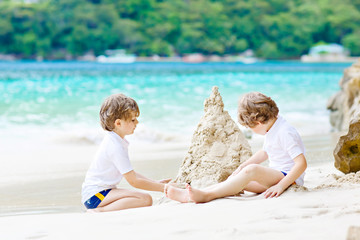 Two kid boys building sand castle on tropical beach