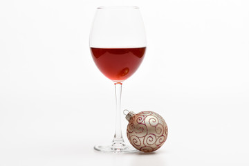 Wineglass with red liquid or wine and christmas ball ornament isolated on white background. Glass with wine and christmas decoration. Winter holidays concept. Winter celebration with alcohol drink