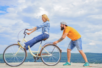 Girl cycling while man support her. Man helps keep balance ride bike. Cycling service. Service and assistance. Mechanic helps maintain bicycle. Supportive service. Woman rides bicycle sky background
