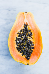 Papaya fruit half with seeds on white marble table top view.