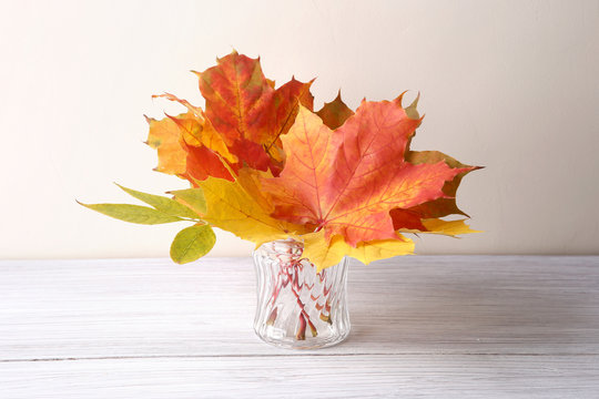 Maple leaves in vase in interior. Autumn colorful composition as decoration indoor.