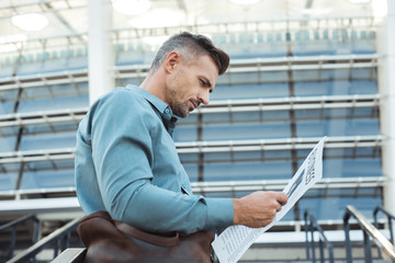 low angle view of handsome middle aged man reading business newspaper on street