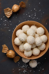 Coconut candies in bowl and wrapped in paper on dark table background flat lay top view