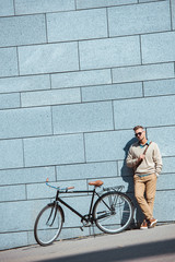 Fototapeta premium handsome stylish middle aged man in sunglasses standing near bicycle on street