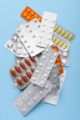 Pills drugs in blisters assortment heap on blue pastel background top view