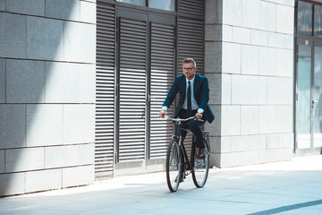middle aged businessman in suit and eyeglasses riding bicycle on street