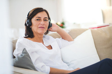 Naklejka premium A senior woman with headphones listening to music at home at Christmas time.