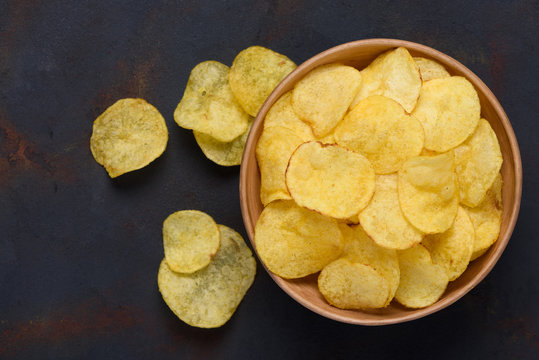 Crispy potato chips in bowl on dark table