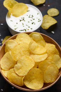 Potato chips in bowl with sauce dip on dark table.