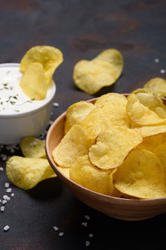 Crispy potato chips in bowl with sauce dip and salt on dark table