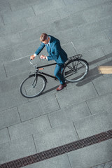 Obraz premium high angle view of businessman in formal wear riding bicycle and checking wristwatch