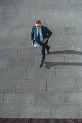 high angle view of businessman with paper cup and newspaper walking on street