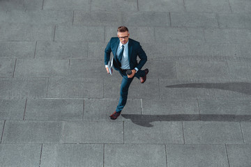 high angle view of middle aged businessman in formal wear holding coffee to go and running on street
