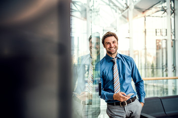 A young businessman with smartphone standing in a modern building, texting.