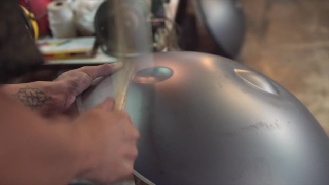 Artisan hands hitting with hammer constructing handpan, a metal percussion instrument.