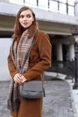 Fashion young woman outdoor. Wearing coat, scarf, and handbag