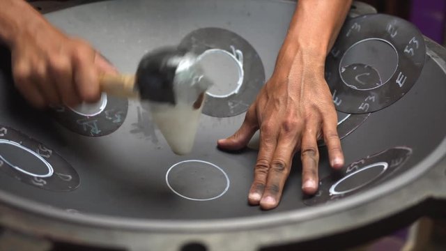 Artisan hands hitting with hammer constructing handpan, a metal percussion instrument.
