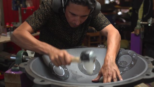 Artisan hands hitting with hammer constructing handpan, a metal percussion instrument.