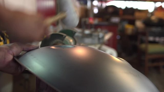 Artisan hands hitting with hammer constructing handpan, a metal percussion instrument.
