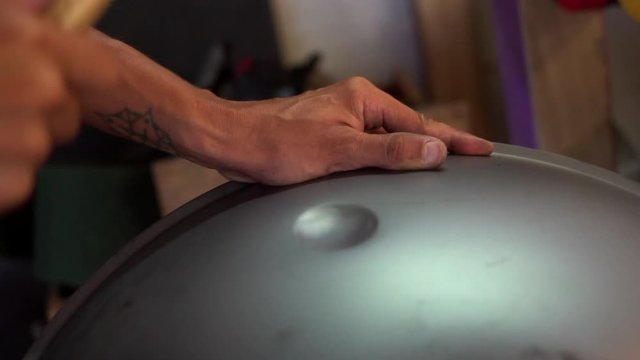 Artisan hands hitting with hammer constructing handpan, a metal percussion instrument.