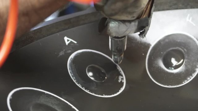 Artisan in his workshop using air hammer to construct a handpan, metal percussion instrument.