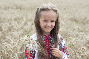 Girl in national costume with embroidery  holding a bouquet of wheat