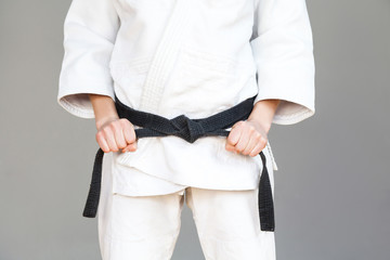 Female fighter torso poses in white kimono and sportive strong arms are closeup black belt....