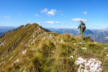 Man hiker walking on top of mountain against blue sky.