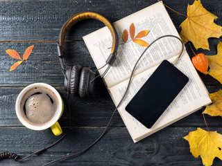 Autumn leaves, coffee, telephone with headphones and audio book concept, modern electronic library