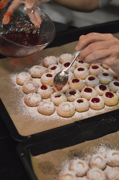 Woman filling warm liquid jam into Christmas cookies that have a hole and are called Engelsaugen or Husarenkrapfen